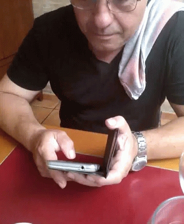 A Man Wearing Glasses And A Black Shirt Is Holding A Cell Phone GIF