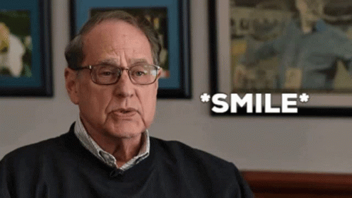 A Man Wearing Glasses And A Black Shirt Is Smiling GIF