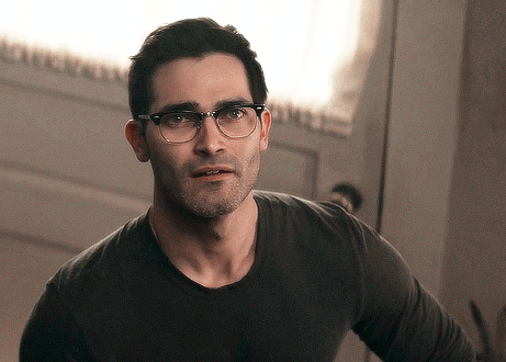 A Man Wearing Glasses And A Black Shirt Is Standing In Front Of A Door GIF