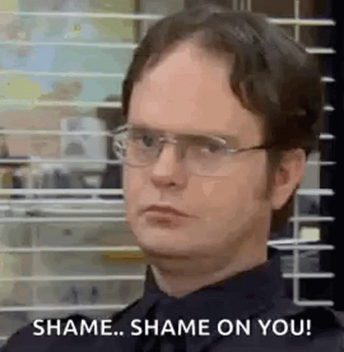 A Man Wearing Glasses And A Black Shirt Is Standing In Front Of A Window With Blinds . GIF