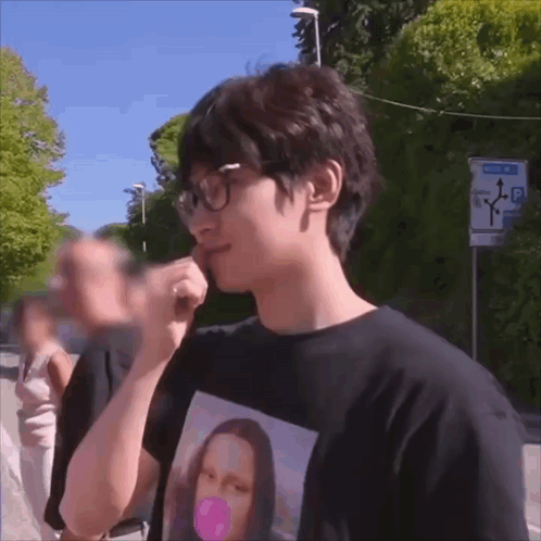 A Man Wearing Glasses And A Black Shirt With A Picture Of Mona Lisa Blowing A Bubble Gum GIF