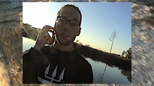 A Man Wearing Glasses And A Black Shirt With The Letter L On It GIF