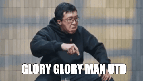A Man Wearing Glasses And A Black Sweatshirt Says Glory Glory Man Utd In White Letters GIF