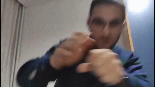 a man wearing glasses and a blue jacket is making a funny face while holding his hands together .