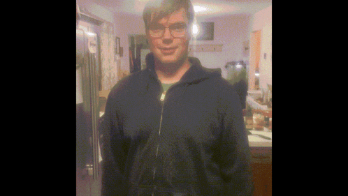 A Man Wearing Glasses And A Blue Jacket Stands In Front Of A Refrigerator GIF