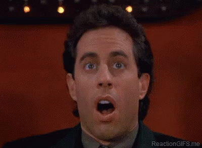 A Man Wearing Glasses And A Blue Shirt Is Laughing With His Mouth Open . GIF