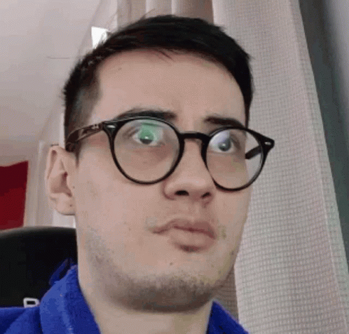 A Man Wearing Glasses And A Blue Shirt Is Making A Face GIF