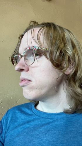 A Man Wearing Glasses And A Blue Shirt Is Making A Face GIF