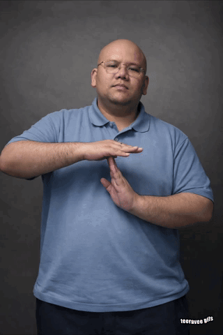 A Man Wearing Glasses And A Blue Shirt Is Making A Gesture With His Hand GIF