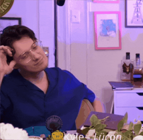 A Man Wearing Glasses And A Blue Shirt Is Sitting At A Table With Kyle Liicon In The Corner GIF