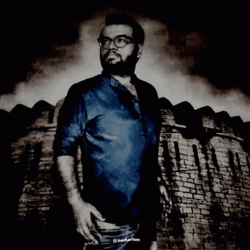 A Man Wearing Glasses And A Blue Shirt Is Standing In Front Of A Brick Wall With The Hashtag Nagkarism GIF