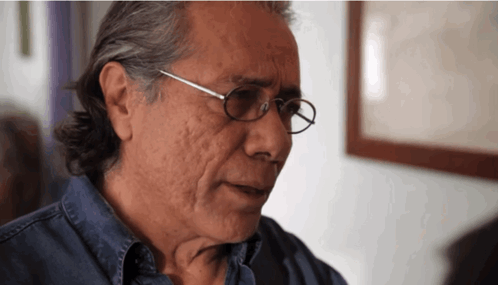 A Man Wearing Glasses And A Blue Shirt Looks At Something GIF