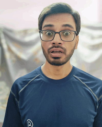 A Man Wearing Glasses And A Blue Shirt With An O On It GIF