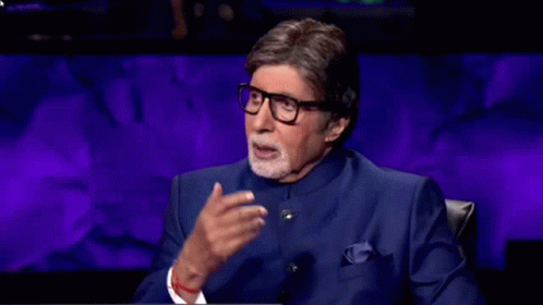 A Man Wearing Glasses And A Blue Suit Is Sitting In Front Of A Purple Wall . GIF