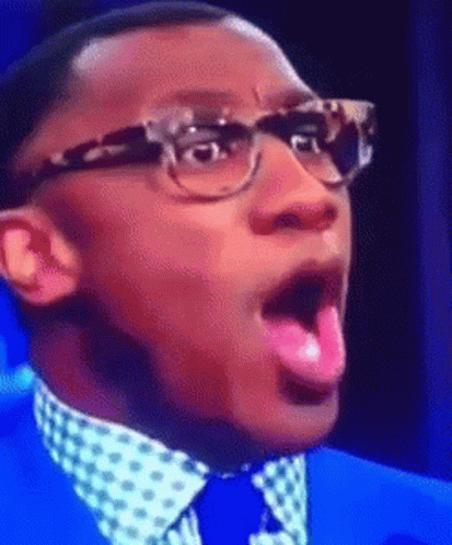 A Man Wearing Glasses And A Blue Suit Is Sticking Out His Pink Tongue GIF