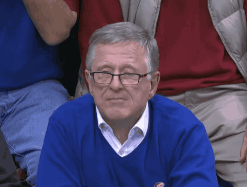 A Man Wearing Glasses And A Blue Sweater Is Sitting In The Audience GIF
