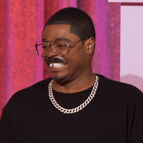 A Man Wearing Glasses And A Chain Around His Neck Is Smiling GIF