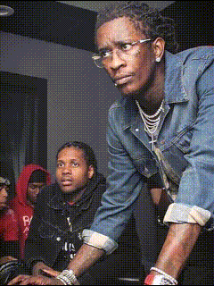 A Man Wearing Glasses And A Denim Jacket Is Standing In A Crowd GIF