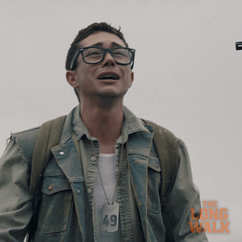 A Man Wearing Glasses And A Denim Jacket With The Long Walk Written On It GIF