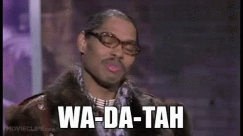 A Man Wearing Glasses And A Fur Coat Is Standing In Front Of A Microphone . GIF
