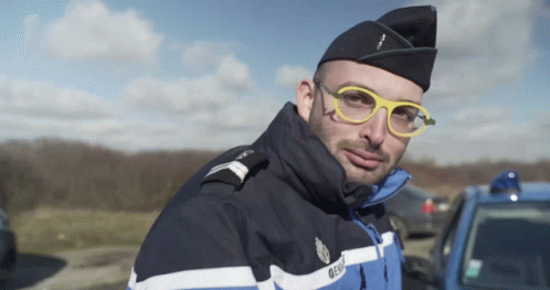 A Man Wearing Glasses And A Gendarmerie Uniform Looks At The Camera GIF