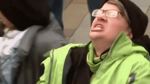 A Man Wearing Glasses And A Green Jacket Is Sitting On A Train . GIF