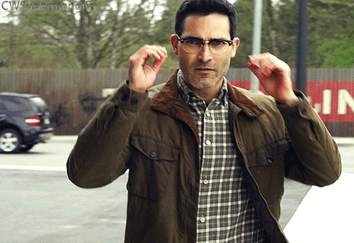 A Man Wearing Glasses And A Green Jacket Is Standing In Front Of A Sign That Says Cws Superman GIF
