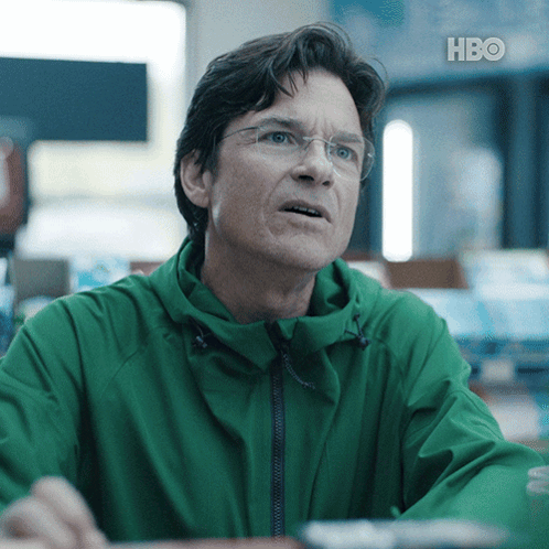A Man Wearing Glasses And A Green Jacket With Hbo Written On The Bottom Right GIF