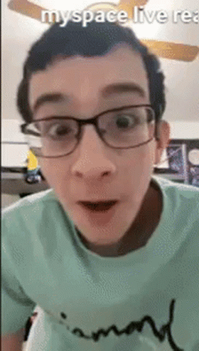 A Man Wearing Glasses And A Green Shirt Is Looking At The Camera . GIF