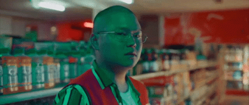 A Man Wearing Glasses And A Green Vest Is In A Store GIF