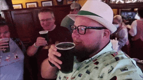 A Man Wearing Glasses And A Hat Is Drinking From A Plastic Cup GIF