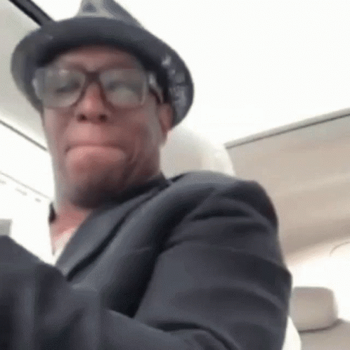 A Man Wearing Glasses And A Hat Is Making A Funny Face . GIF