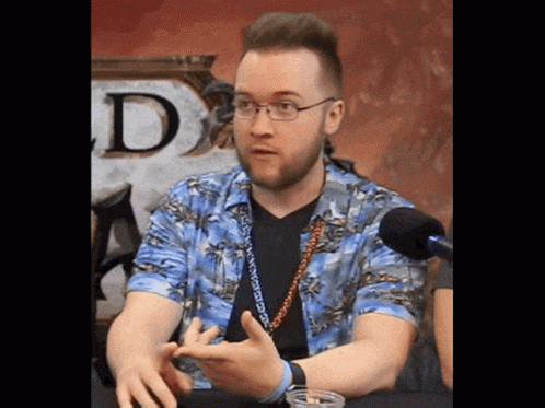 A Man Wearing Glasses And A Hawaiian Shirt Is Sitting In Front Of A Microphone GIF