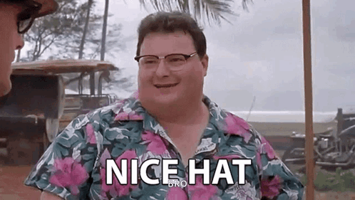 a man wearing glasses and a hawaiian shirt is smiling and saying `` nice hat `` .