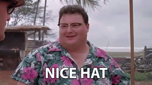 a man wearing glasses and a hawaiian shirt is standing next to another man and saying `` nice hat '' .