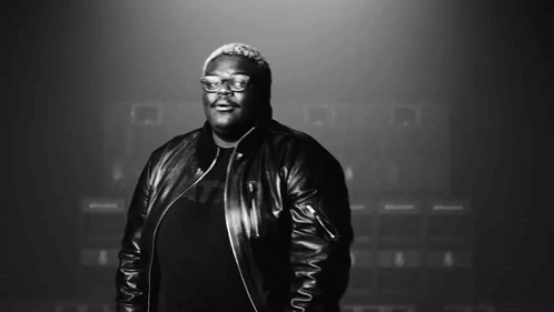 A Man Wearing Glasses And A Leather Jacket Smiles In A Black And White Photo GIF