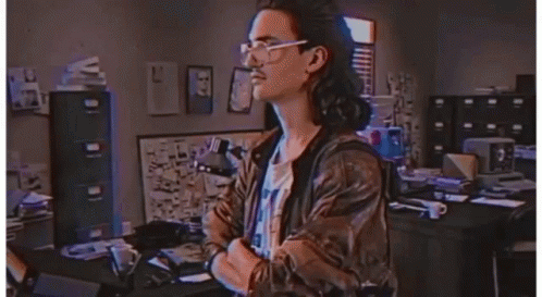 A Man Wearing Glasses And A Leather Jacket Stands In Front Of A Sign That Says Hackerman GIF
