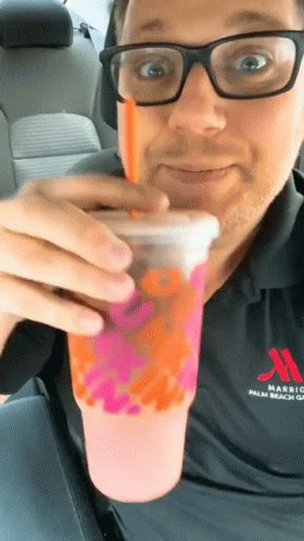 A Man Wearing Glasses And A Marriott Shirt Drinks A Pink Drink GIF