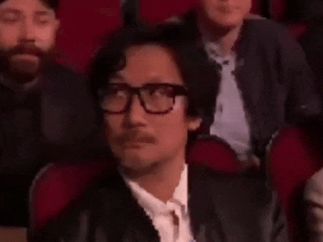 A Man Wearing Glasses And A Mustache Is Sitting In A Theatre . GIF