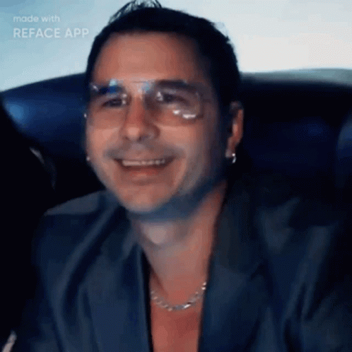 A Man Wearing Glasses And A Necklace Is Smiling In A Video Made With Reface App GIF