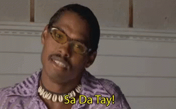 A Man Wearing Glasses And A Necklace Is Smiling With The Words `` Sa Da Tay '' Behind Him . GIF