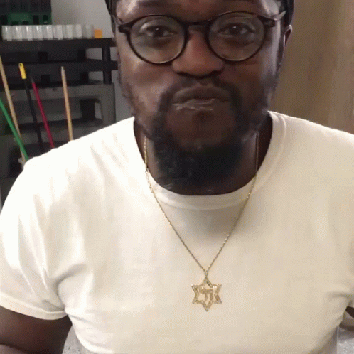 A Man Wearing Glasses And A Necklace With A Star Pendant GIF