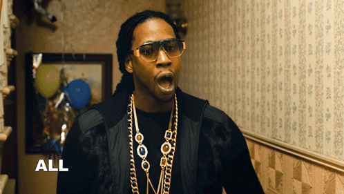 A Man Wearing Glasses And A Necklace With The Word All Behind Him GIF