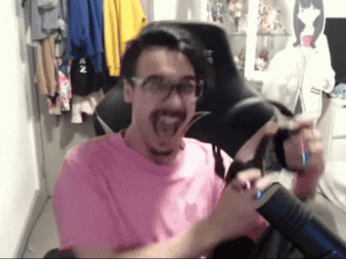 A Man Wearing Glasses And A Pink Shirt Is Sitting In A Chair With His Mouth Open GIF
