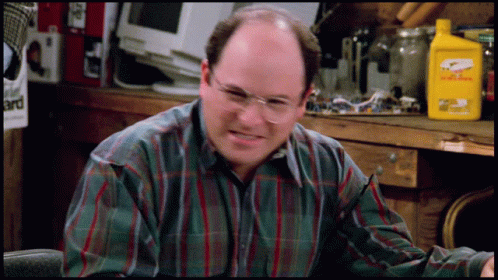 A Man Wearing Glasses And A Plaid Shirt Is Sitting In Front Of A Table With A Yellow Bottle That Says Eagle One GIF
