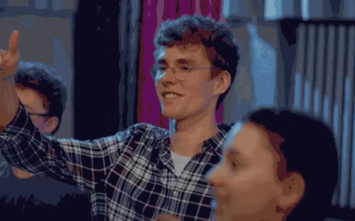 A Man Wearing Glasses And A Plaid Shirt Is Smiling And Giving A High Five GIF