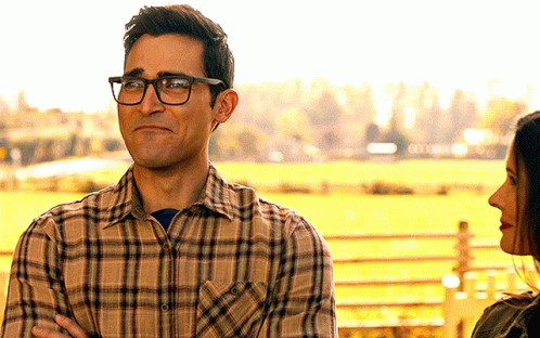 A Man Wearing Glasses And A Plaid Shirt Looks At A Woman In A Field GIF