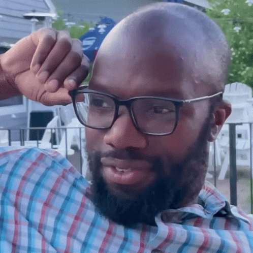 A Man Wearing Glasses And A Plaid Shirt Wipes His Forehead With His Hand GIF
