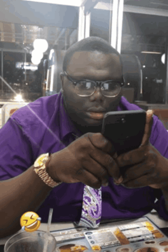 A Man Wearing Glasses And A Purple Shirt Is Looking At His Phone GIF