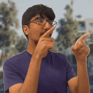 A Man Wearing Glasses And A Purple Shirt Is Pointing At The Camera GIF